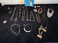 Full lot of costume jewelry laid out on black fabric showing all necklaces, bracelets, and earrings in the lot.