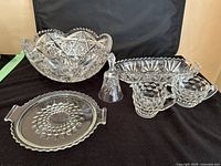 Wide shot of all crystal cut glass items included in the lot showing the large centrepiece bowl, serving bowl, bell, creamer and sugar containers, and platter.