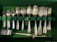 Top view showing an assortment of spoons, forks, and serving utensils in a green felt flatware chest.