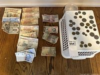 Coins and paper money arranged on floor and plastic basket.