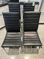 Front view of four black leatherette chairs with chrome legs, showing overall style and condition.