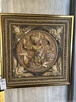 Front view of framed Asian textile artwork showing detailed fabric applique, sequin embellishments, and ribbon work surrounding a central figure and corner faces.