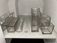 Photo showing eight clear glass vases and planters of various shapes and sizes arranged on a white shelf.