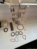 Overview showing earring holder with multiple earrings and laid out bracelets and necklaces on a white surface.