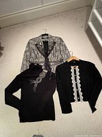 Three ladies clothing items including a patterned blazer, black turtleneck sweater with rhinestone design, and black lace trimmed cashmere sweater.