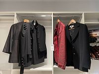 Four ladies clothing items hanging in closet: black suit, Lida Baday black coat, Jenne Maag red suit jacket, and black jacket made in France.