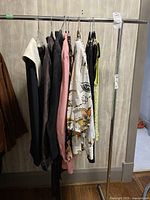 Side view of clothing rack with five garments including jackets, blouses, and other items.
