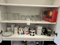 Bottom shelf showing collection of coffee mugs with various designs and three small plates