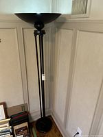 Full view of the modern black metal floor lamp showing the upright design, black shade, and base with triple supports.