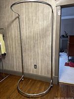 Full view of chrome adjustable clothing rack with oval base and curved top bar.