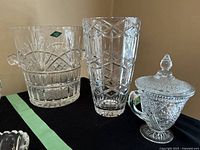 Photo showing three crystal pieces including an ice bucket with side handles, a tall cross and olive vase, and a sugar bowl with lid.