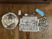 Photo showing silver plate serving tray, assorted flatware including knives, forks, spoons, and serving utensils.