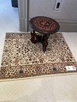 Photo of small Oriental style rug with floral pattern and small round Asian style occasional table placed on top.
