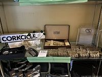 Photo of Supreme Cutlery utensil set in box, gold-tone decorative place-card holders, Corkcicle box, clear acrylic serving trays and black baskets arranged on a table.