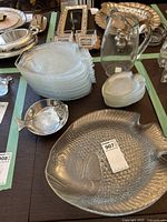 Wide view of the lot showing the large metal fish platter, stacked large glass plates, smaller fish-shaped glass plates, and clear glass water jug