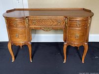 Front view showing full desk with curved front, two pedestal sections each with three drawers, brass ring pulls and decorative brass accents on corners and legs.