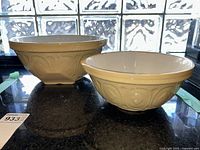 Two cream-colored vintage ironstone mixing bowls by T.G. Green Ltd., sizes 15D and 10D, with embossed exterior patterns, placed on a dark countertop.