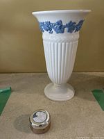 Front view of the white Wedgwood vase showing vertical ribbing and blue floral relief near rim with small Wedgwood candle case in front of it.