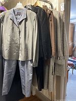 View of various women's coats and pant suits on hangers, showing different styles and fabrics including satin and wool.