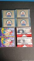 Six cassette tapes arrayed flat on a black surface: four 20th Century Music tapes in beige and blue packaging, two colorful Rockabilly cassette packages, two white Certron blank dictation cassette tapes in plastic cases with red and white labels.