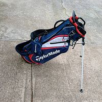 Side view of the TaylorMade golf bag standing with legs extended on concrete surface showing big side pocket and branding.