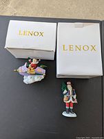 Two vintage Lenox Christmas figurines with their original Lenox boxes on a black surface.