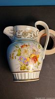 Pitcher showing floral design and handle, placed next to roll of tape for size reference.