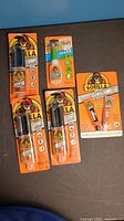 Photo of five Gorilla glue packages including epoxy, super glue, and steel bond epoxy, all new in original orange packaging with gorilla logo