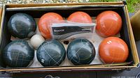 Overhead view of the bocce set showing 8 bocce balls in total (4 black, 4 orange), 1 white pallino ball, and boxed game rules inside original cardboard box.
