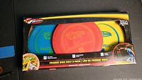 Top view of the original retail packaging containing three disc golf frisbees in red, yellow, and blue colors with Whamo branding and graphics.
