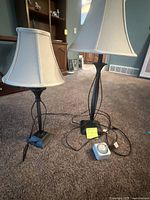 Two small metal lamps with white fabric shades on carpeted floor, one 26 inches and the other 32 inches tall, showing lamp bases and cords