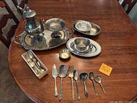 Full table view showing teapot on large silver platter, two sterling silver bowls, several silver plated bowls and a box with cutlery including sterling silver cocktail fork.