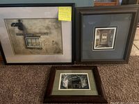 Three framed pictures arranged on carpet: two standing against wall, one lying flat.