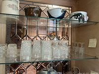 Glassware displayed on glass shelves inside a cabinet. Includes small and medium textured glasses and wine glasses. Clear glass with diamond hobnail pattern visible.