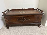 Front view of the antique wooden hope chest showing detailed carved design, handle bars, surface wear and nicks on corners