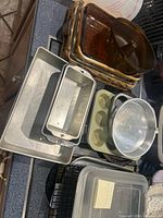 Stack of various metal and glass baking pans, muffin trays, cooling racks, and casserole dishes on a counter.