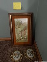 Full view of the rectangular bird painting and two small oval bird paintings with gold ornate frames on floor against wall.