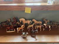 Multiple horse and donkey ceramic and porcelain figurines arranged on a wooden surface showing variety in size and color.
