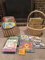 Two wicker baskets filled with children's books, placed in front of a fireplace, with some books arranged lying down to show titles.