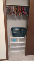 Closet interior showing the plastic storage bin unit with laundry basket on top and metal rod with assorted colored hangers