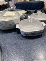 Five small CorningWare baking dishes shown on a counter with colorful floral and blue designs and matching lids.
