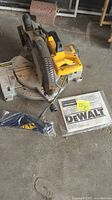 Overview of the DeWalt 10" compound miter saw with instruction manual and unused wood shavings catcher laid on the floor showing the entire saw and accessory placement.