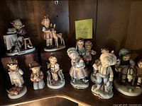 Multiple child figurines arranged on shelf, including two on wooden pedestals.