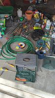 Photo showing assorted gardening tools, hoses, garden wires, a metal toolbox, and pots on the garage floor