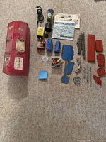 Overview of Erector set components and original red metal toolbox laid out on carpeted floor.