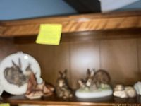 Shelf with Goebel rabbit bas relief plate on left and multiple rabbit figurines arranged on wood shelf.