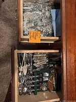 Drawer filled with wrapped glassware and a separate drawer with organized Oneida Michelangelo flatware pieces including forks, knives, spoons, and serving utensils.