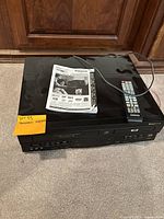 Front and top view of the Panasonic PV-D4742 DVD/VCR combo deck with remote control and manual on top.