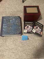 Photo showing the blue patterned photo album, the wooden Showbox photo viewer, and two unopened boxes of replacement film reels, with a small sign stating 'New Unused Photo Album Showbox'