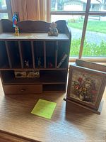 Front view of the wooden desk shadow box with small figurines placed in compartments and a drawer, along with the wooden holder featuring pressed flowers.